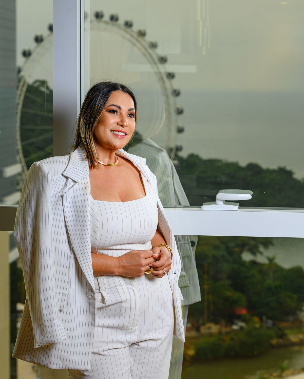 Retrato profissional feminino em ambiente interno de apartamento à venda, com a roda-gigante de Balneário Camboriú ao fundo.