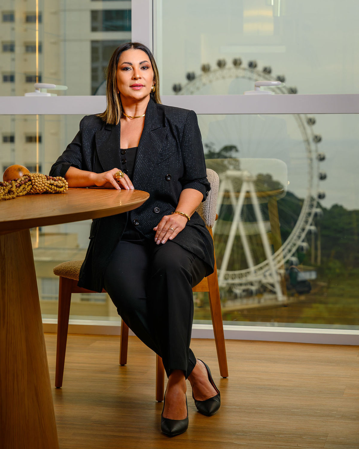 Retrato profissional de corretora de imóveis sentada em ambiente corporativo com vista para a roda-gigante de Balneário Camboriú ao fundo.