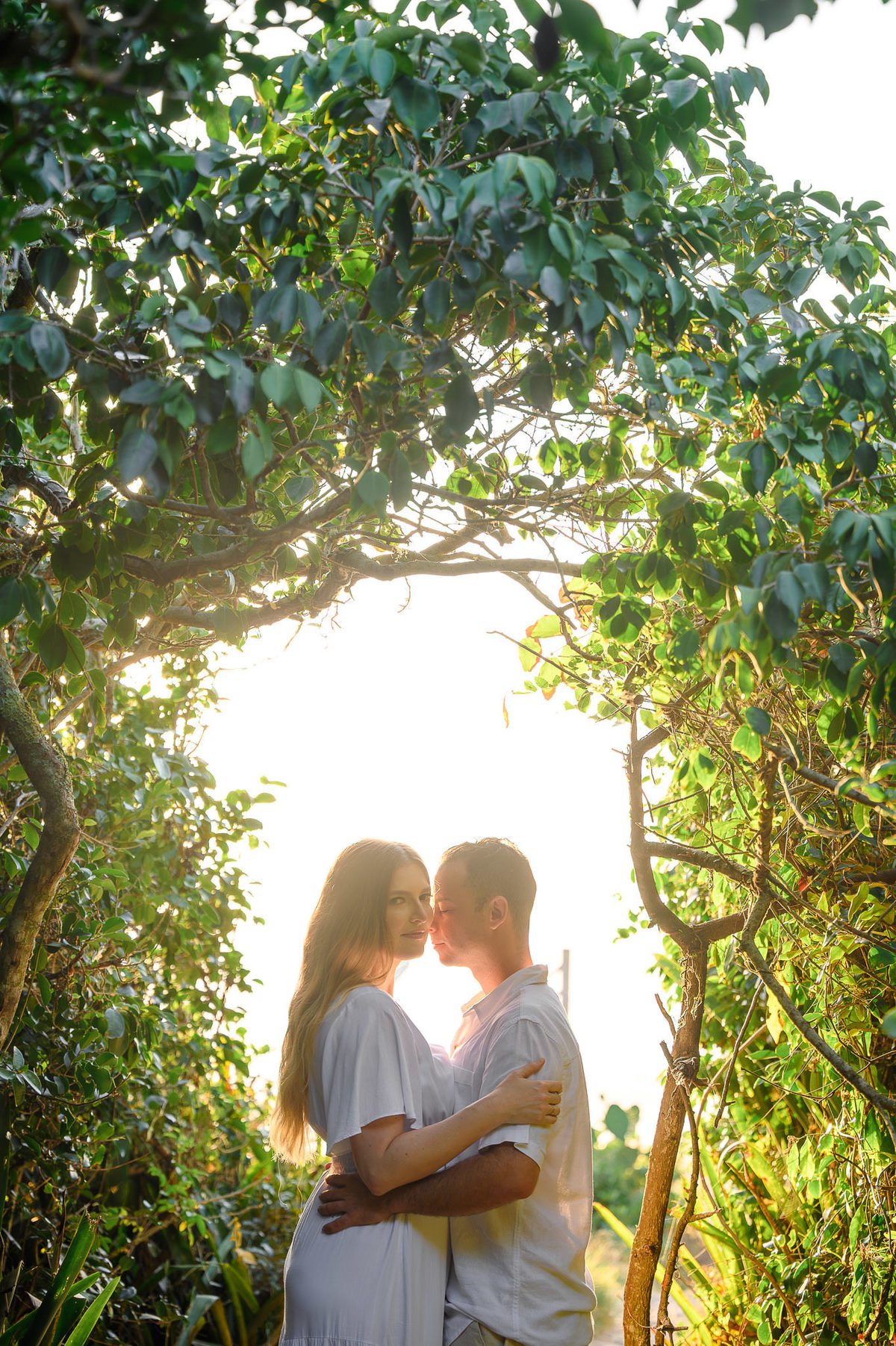 Casal abraçado em trilha no meio da vegetação, com luz suave atravessando as folhas no início da manhã, ensaio pré-wedding em Balneário Camboriú, SC