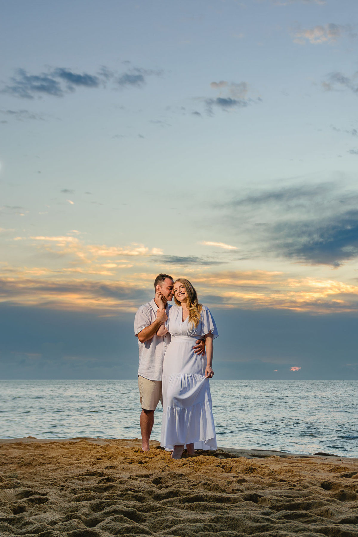 Casal em pé na areia da praia ao amanhecer, com céu amplo e tons suaves ao fundo, ensaio pré-wedding em Balneário Camboriú, SC