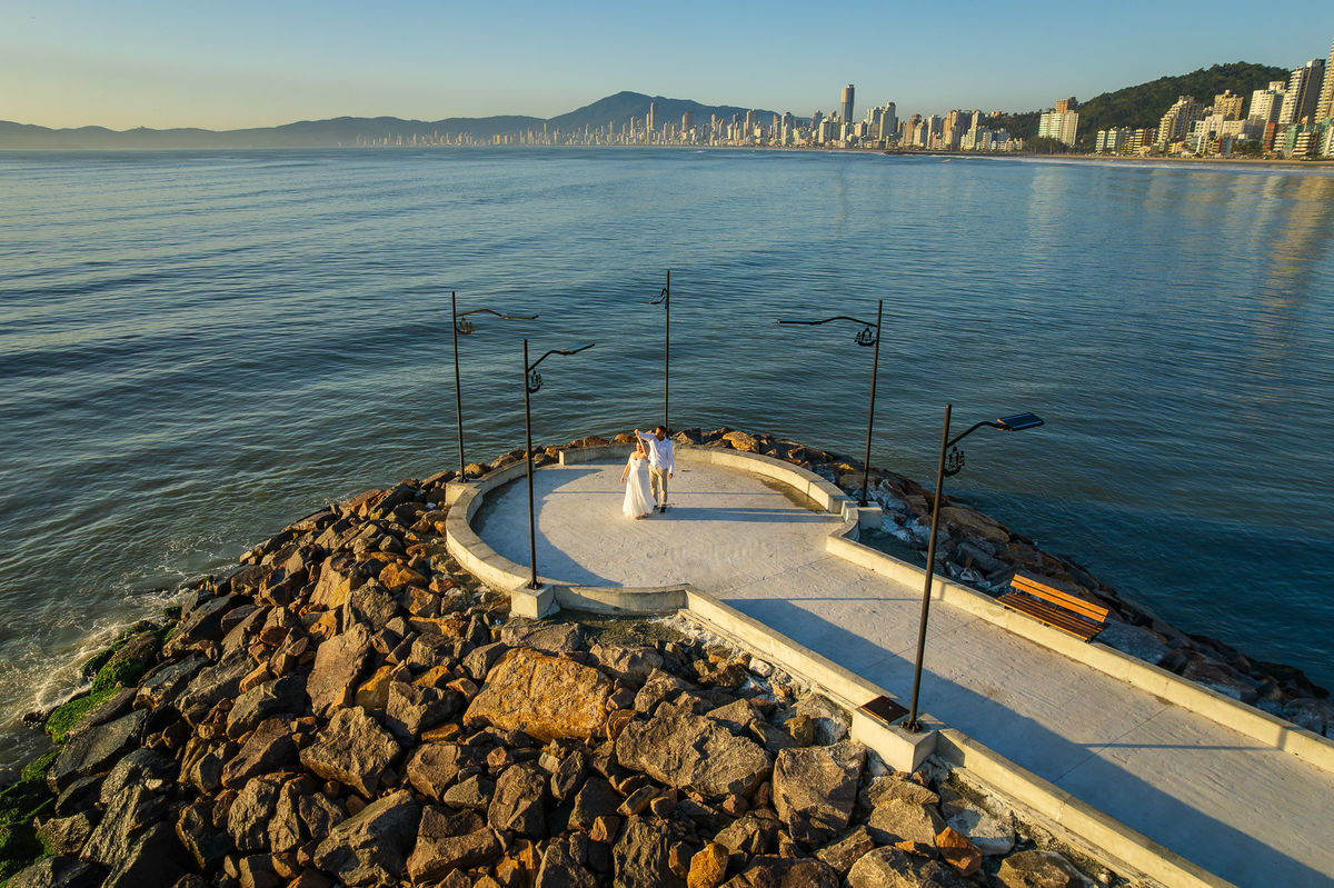 Casal em ensaio pré-casamento em mirante à beira-mar em Balneário Camboriú, SC, fotografado por drone com o mar calmo ao fundo