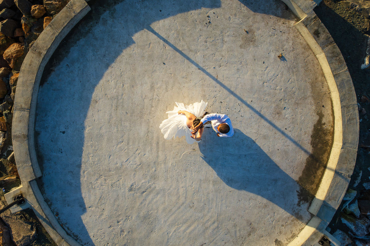 Vista aérea de ensaio pré-wedding de casal em estrutura circular no molhe em Balneário Camboriú, Santa Catarina, durante a luz dourada