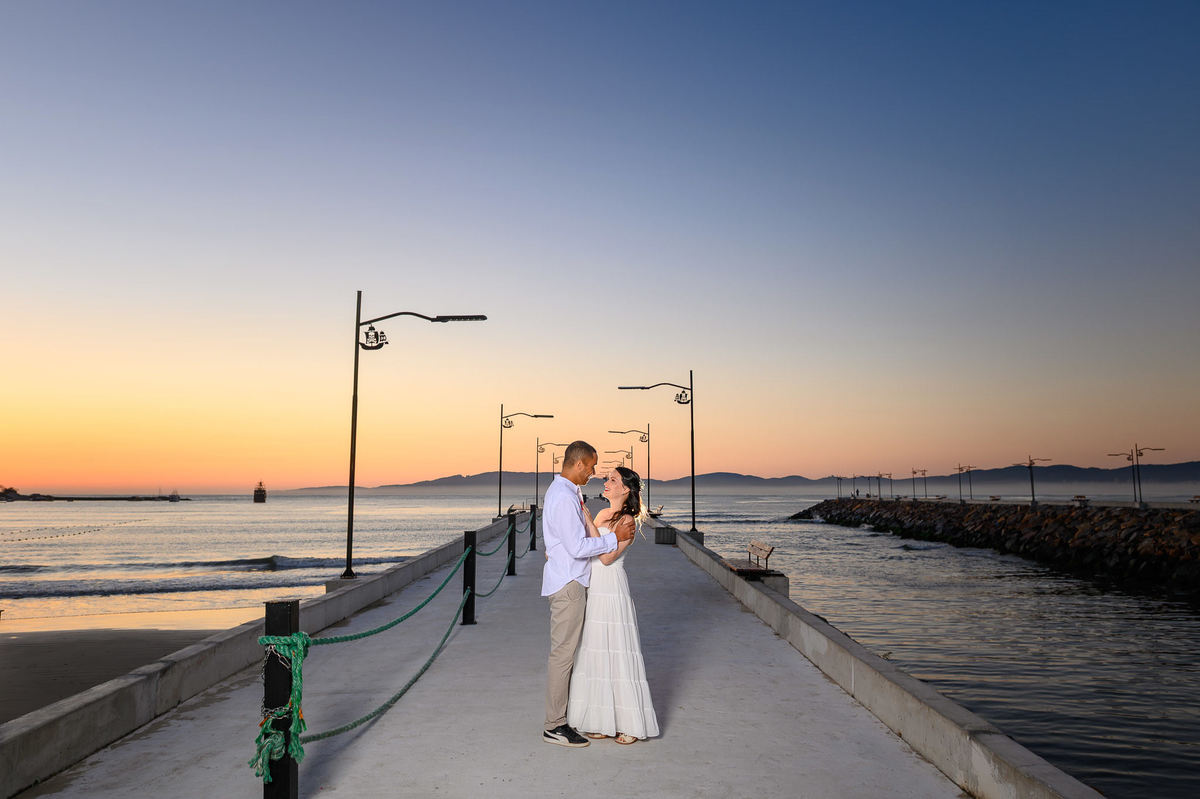Ensaio pré-wedding de casal no mirante do molhe em Itapema, Santa Catarina, com skyline da cidade ao fundo ao amanhecer