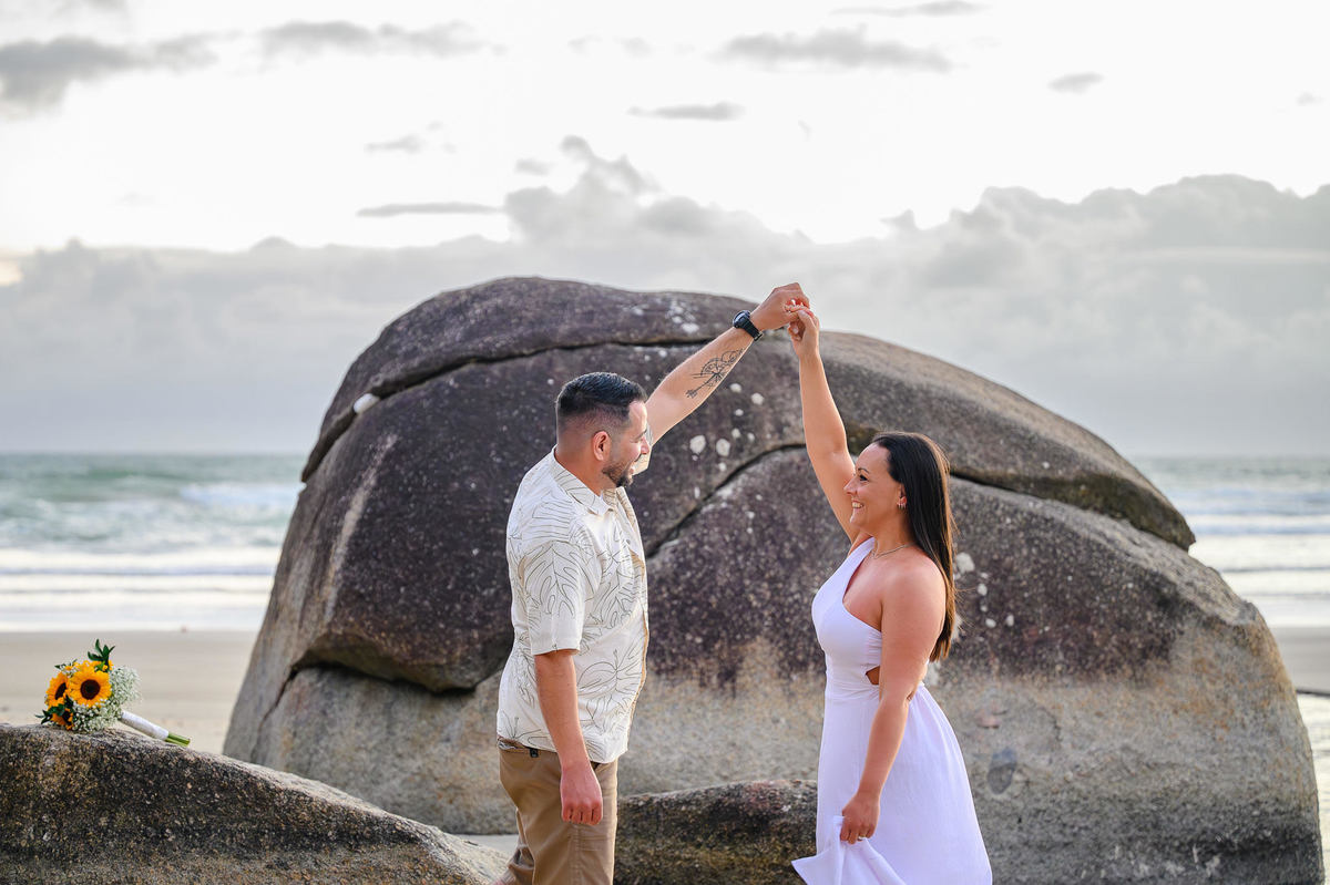 Casal girando e se divertindo em frente às rochas em Bombinhas SC, ensaio fotográfico de casal na praia