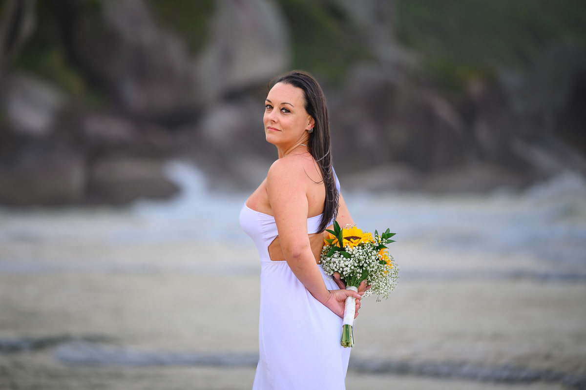 Ensaio de casal em Bombinhas SC com buquê de girassóis, fotografia romântica na praia de Santa Catarina