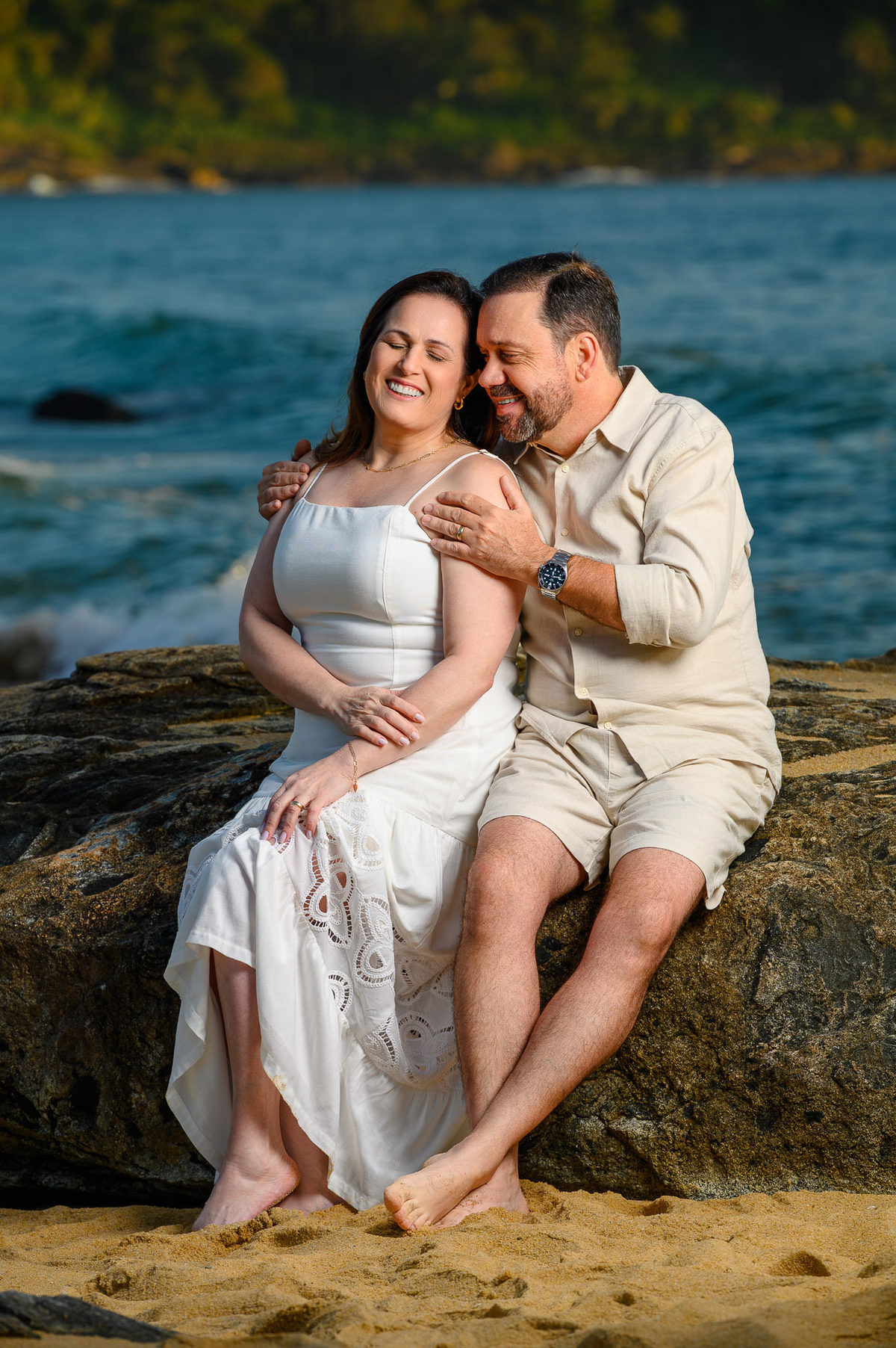 Casal sentado nas pedras durante ensaio de família na Praia do Estaleirinho em Balneário Camboriú