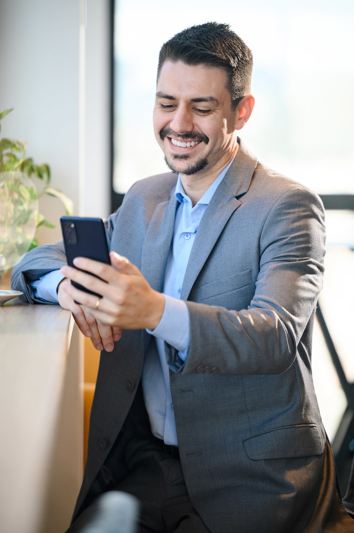 Close em retrato corporativo de advogado utilizando smartphone em ambiente corporativo moderno com iluminação natural em Balneário Camboriú.