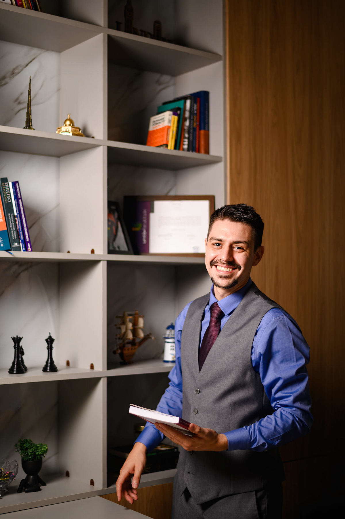 Retrato corporativo profissional de advogado em escritório com estante de livros ao fundo, fotografia de posicionamento profissional em ambiente interno.