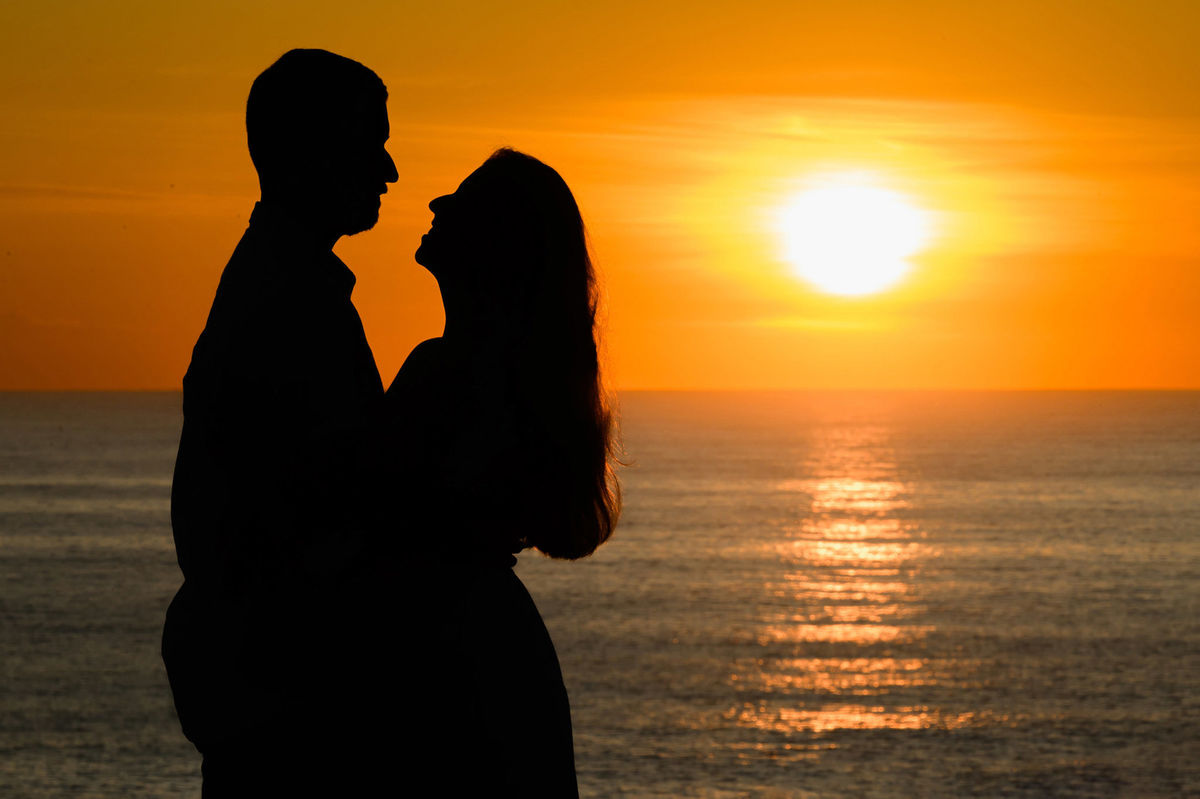 Silhueta do casal de frente para o sol baixo no horizonte na Praia de Taquarinhas, em Balneário Camboriú, no ensaio pré-wedding