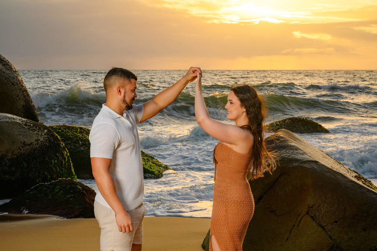 Casal em ensaio pré-casamento na Praia de Taquarinhas, Balneário Camboriú, com mar e pedras ao fundo