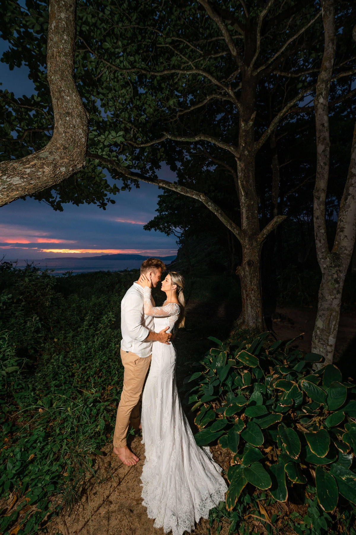 Noivos se abraçando durante ensaio pré-wedding ao amanhecer na praia de Itapema, com céu colorido da manhã e paisagem natural.