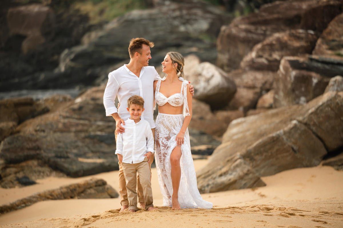 Família sorrindo durante ensaio pré-wedding ao amanhecer na praia em Itapema SC, com céu claro da manhã e clima leve.