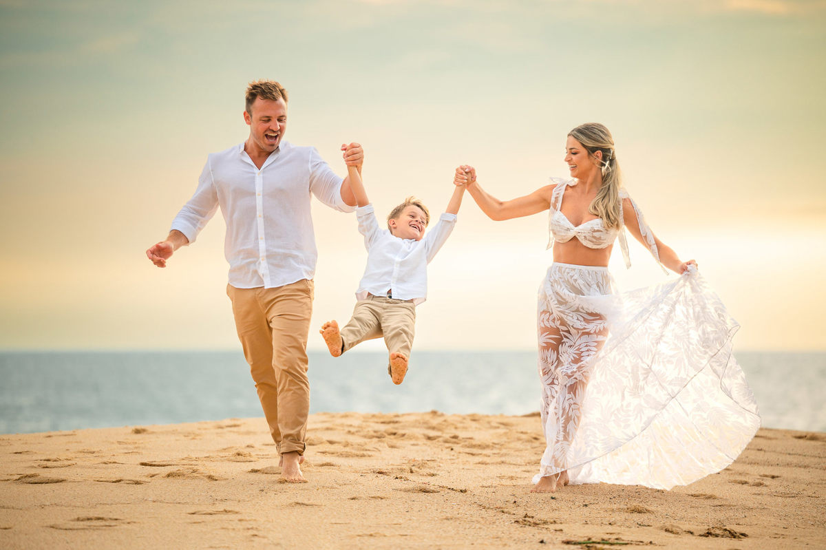 Família em ensaio pré-wedding ao amanhecer na praia em Itapema SC, com casal e filho caminhando na areia com luz suave da manhã.
