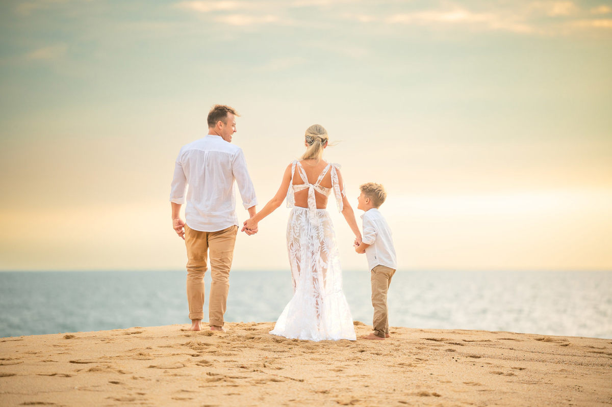 Família em ensaio pré-wedding ao amanhecer na praia em Itapema SC, com casal e filho caminhando na areia com luz suave da manhã.