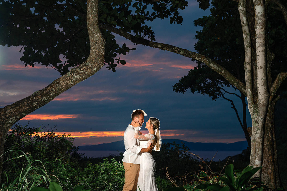 Noivos se abraçando durante ensaio pré-wedding ao amanhecer na praia de Itapema, com céu colorido da manhã e paisagem natural.