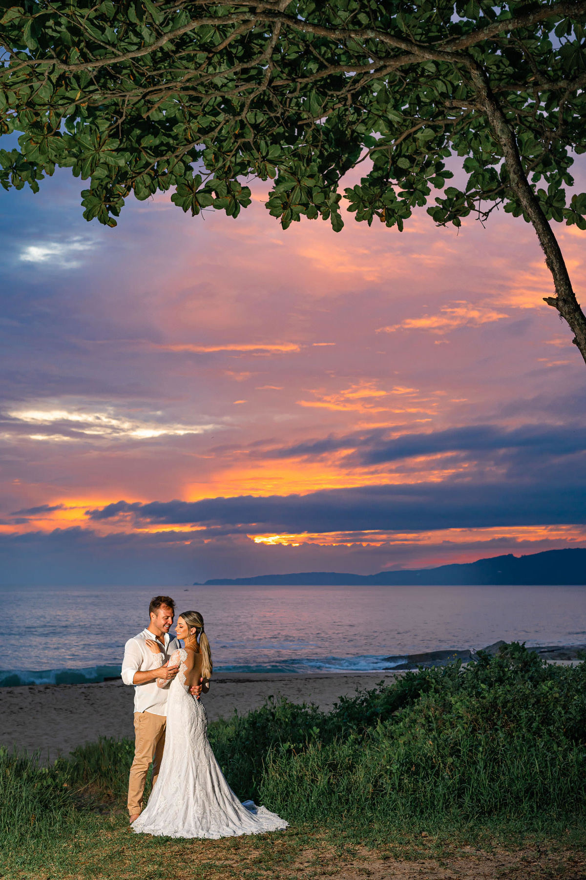Casal em ensaio pré-wedding ao amanhecer na praia em Itapema SC, em meio à natureza, com luz suave da manhã e mar ao fundo.