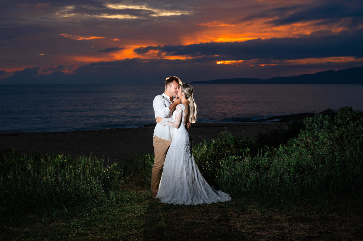 Noivos se abraçando durante ensaio pré-wedding ao amanhecer na praia de Itapema, com céu colorido da manhã e paisagem natural.