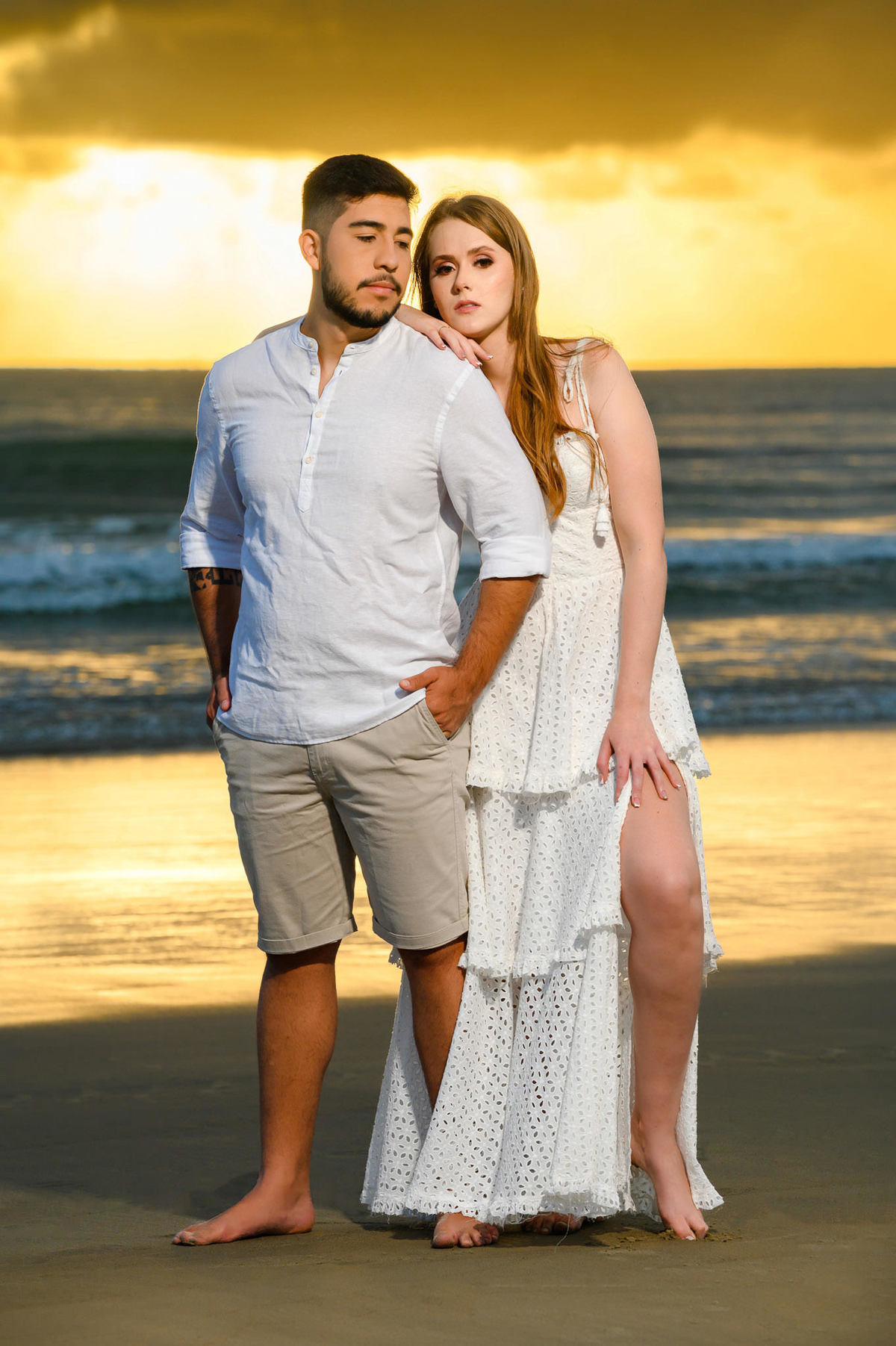 Retrato do casal posado de frente para o mar ao amanhecer na praia de Bombas em Bombinhas, com céu iluminado pela luz da manhã