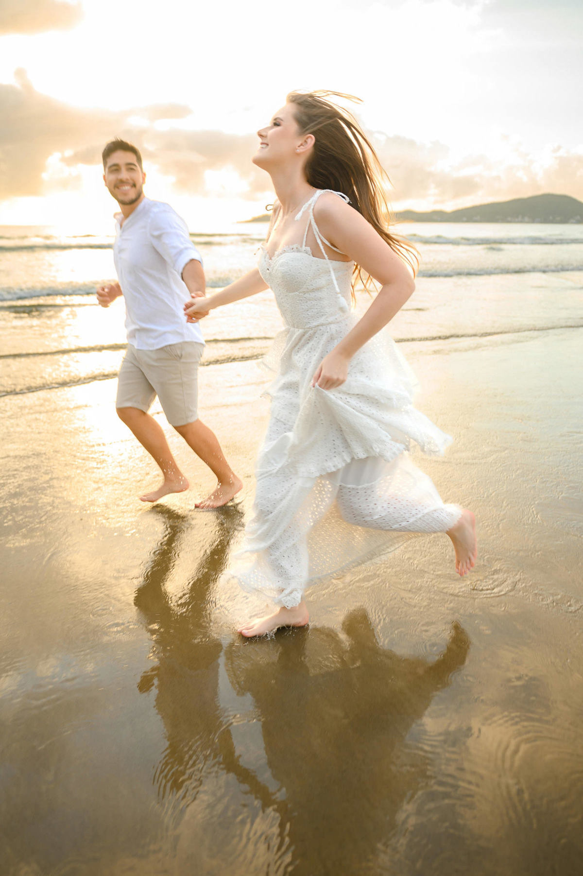 Casal correndo de mãos dadas na beira do mar durante ensaio pré-wedding ao amanhecer em Bombinhas, SC, com movimento e leveza