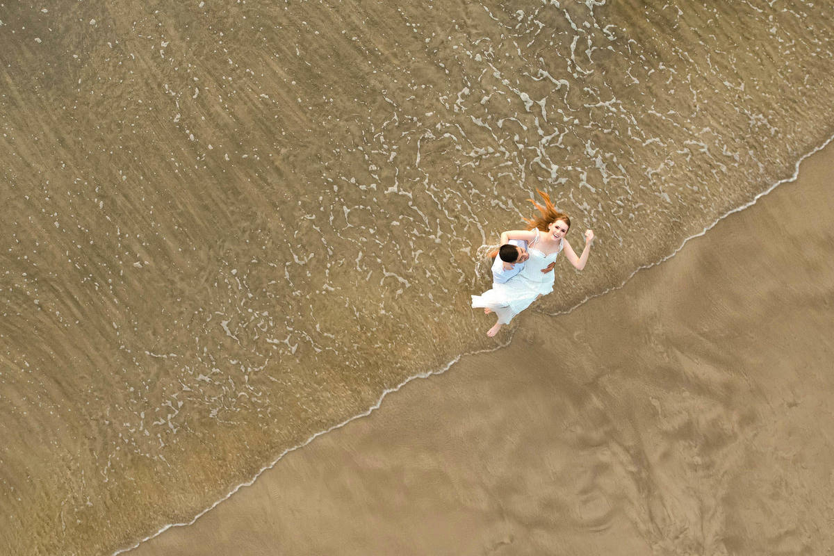 Foto aérea de drone do casal caminhando na areia molhada ao amanhecer na praia de Bombas em Bombinhas, Santa Catarina.