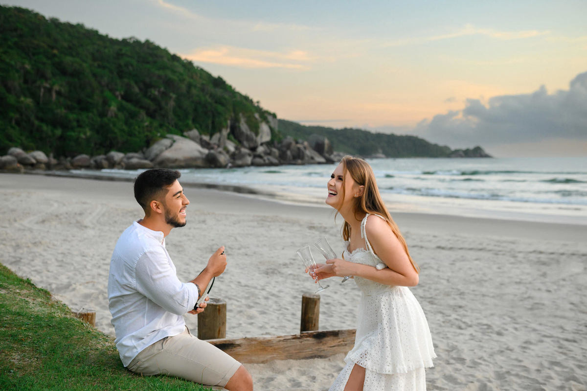 Pedido simbólico com espumante durante ensaio pré-wedding ao amanhecer na praia de Bombas em Bombinhas, Santa Catarina