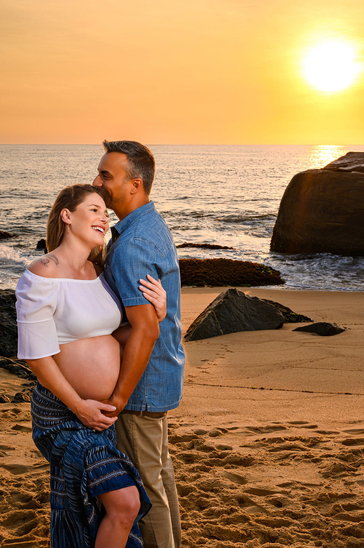 Ensaio gestante ao amanhecer na praia do Estaleirinho, em Balneário Camboriú SC, casal abraçado em momento de carinho com o sol refletindo no mar