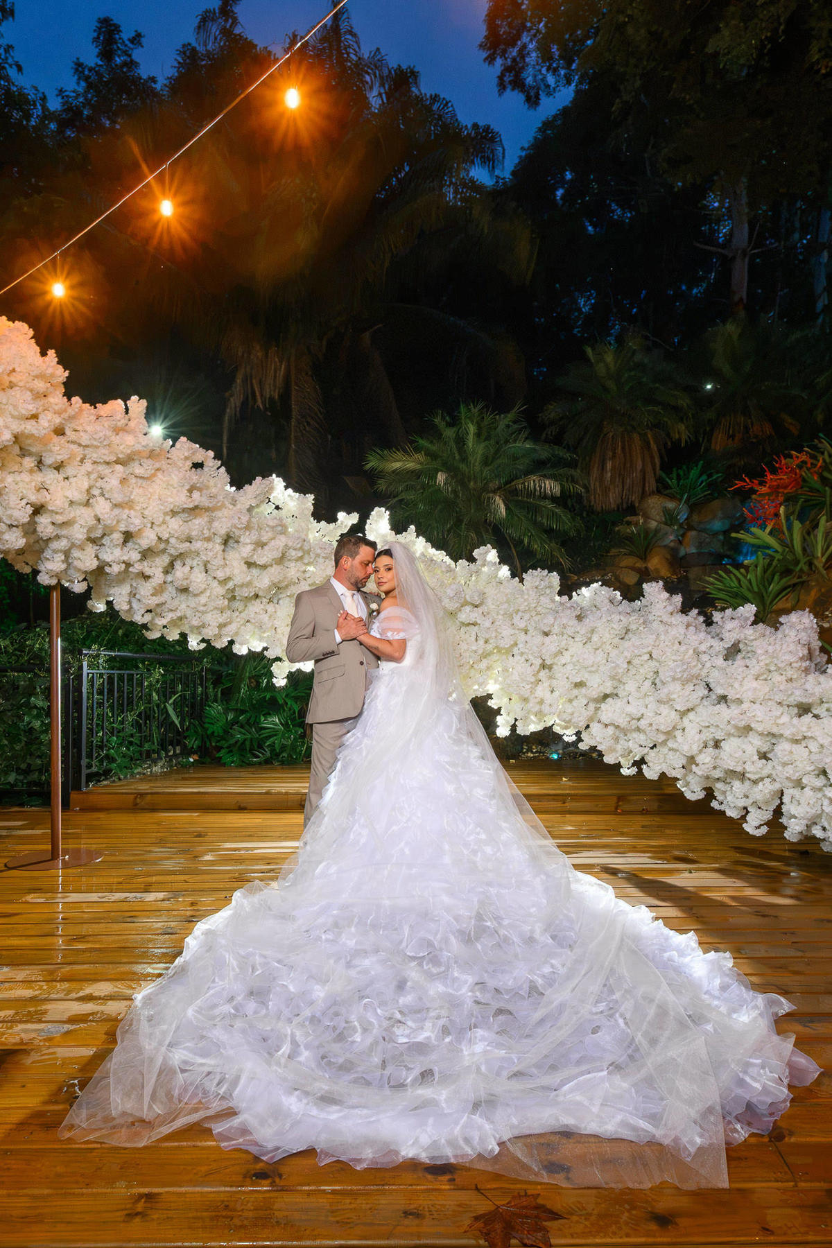 Casal no Espaço Cascata com a cauda do vestido e as luzes refletidas no deck molhado.