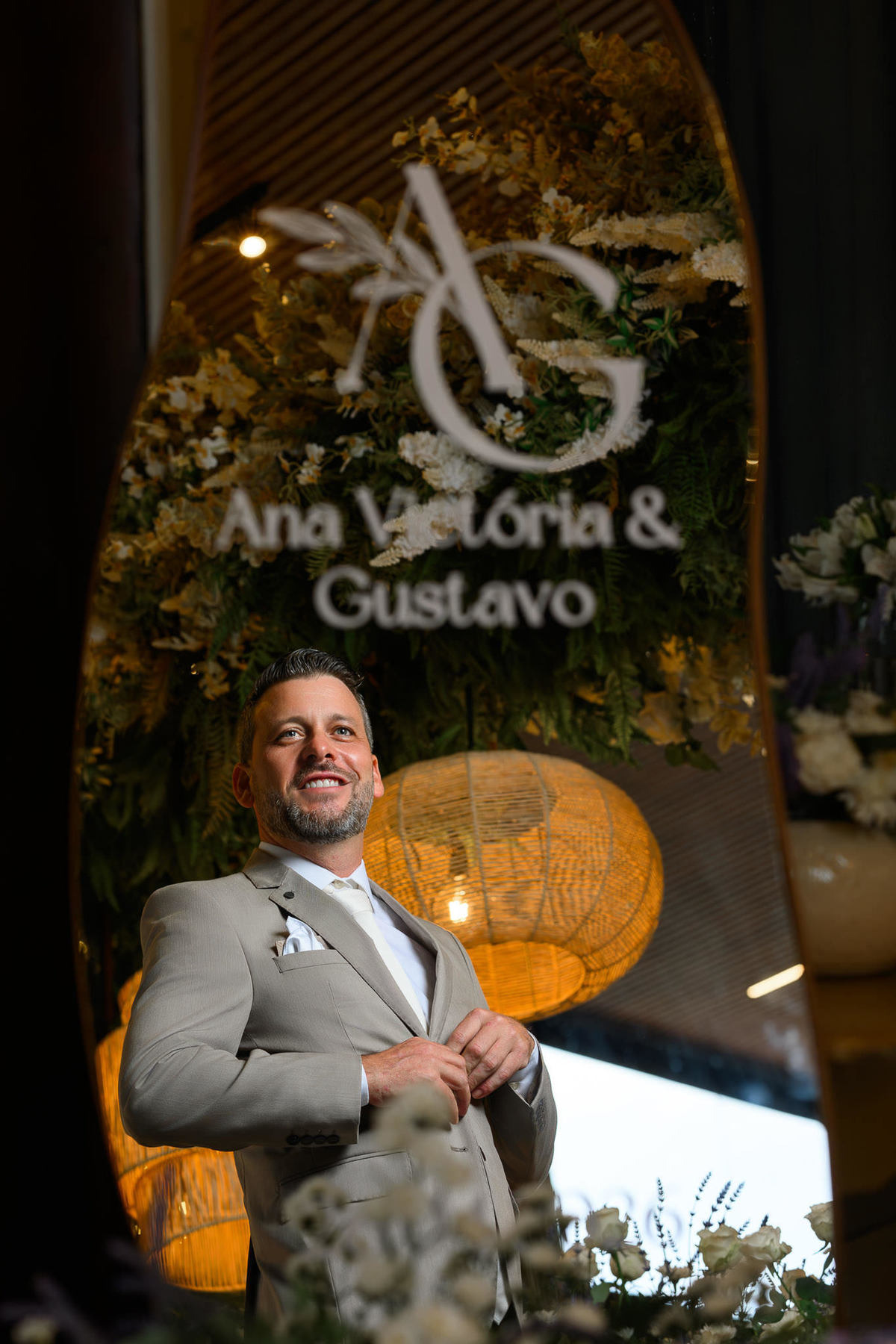 Noivo ajusta o paletó diante do espelho personalizado com as iniciais do casal.