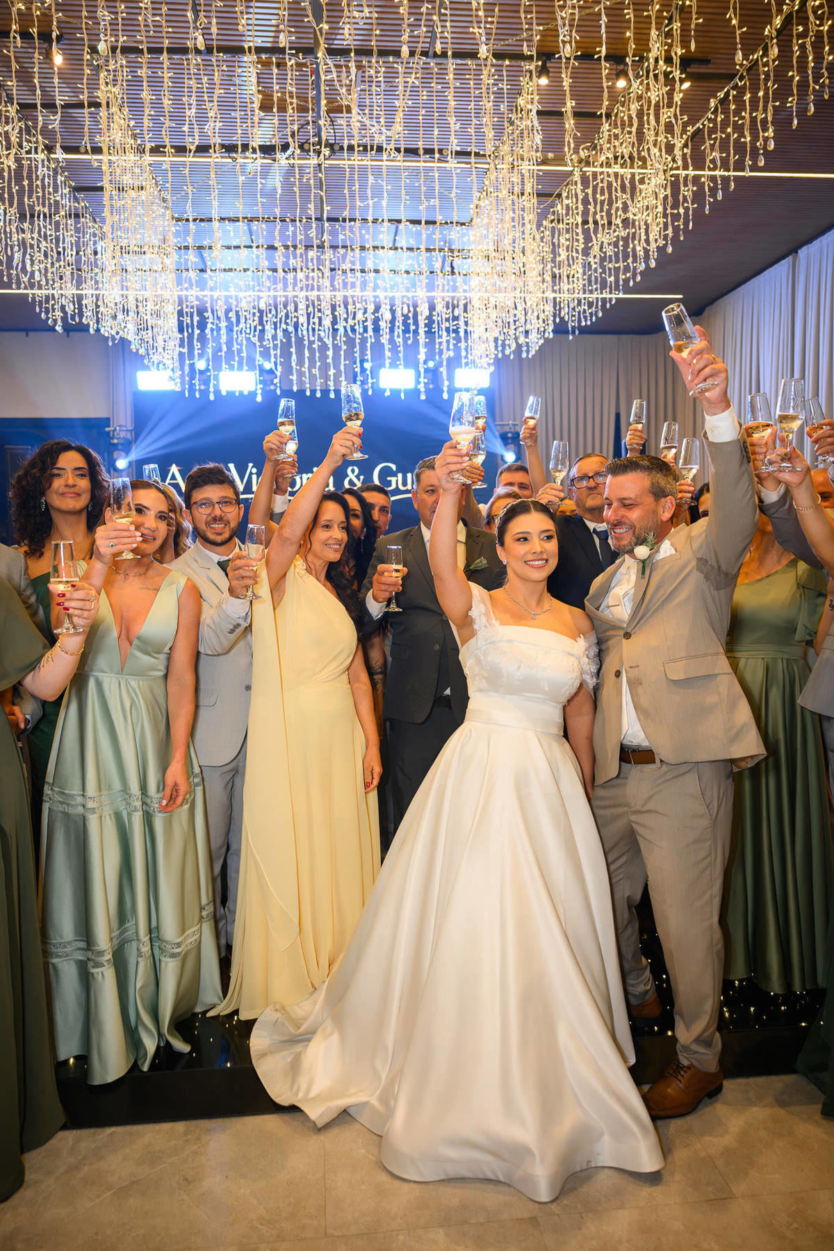 Noivos e convidados brindam sob o teto de luzes do salão do Indaiá Eventos.