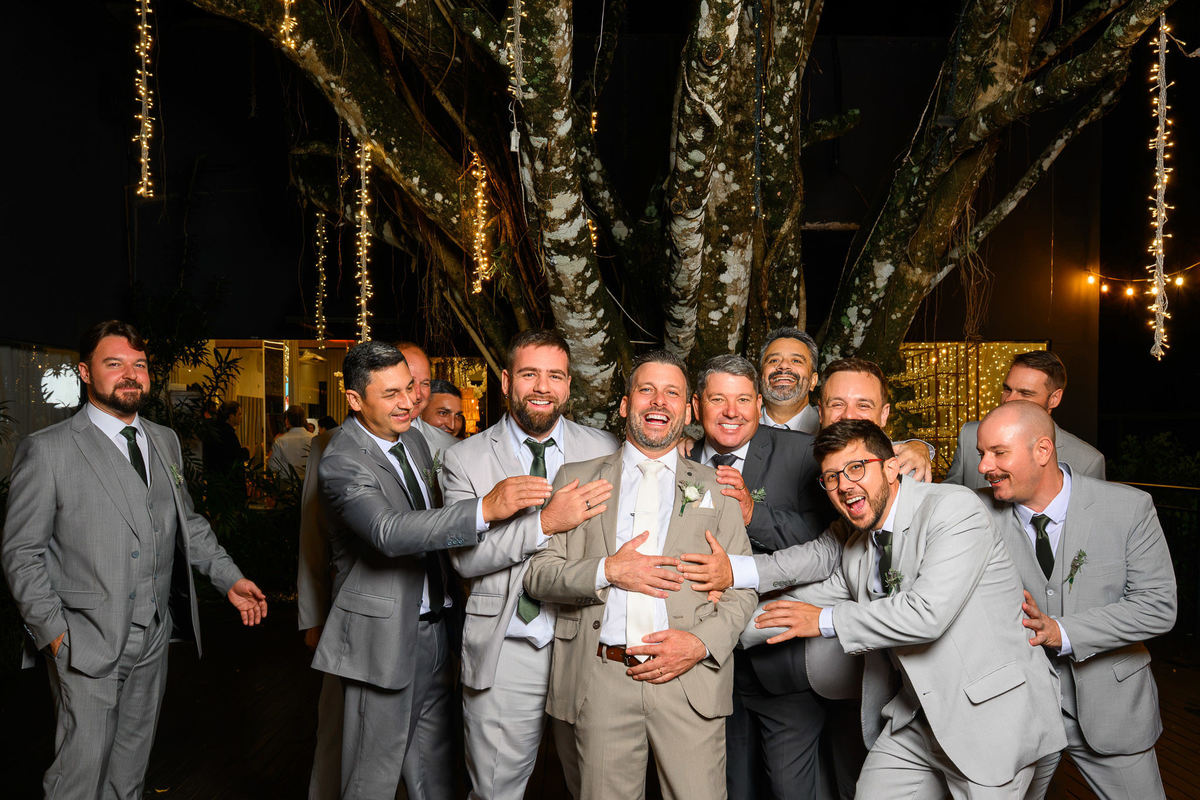 Noivo ri cercado pelos amigos durante a festa de casamento.