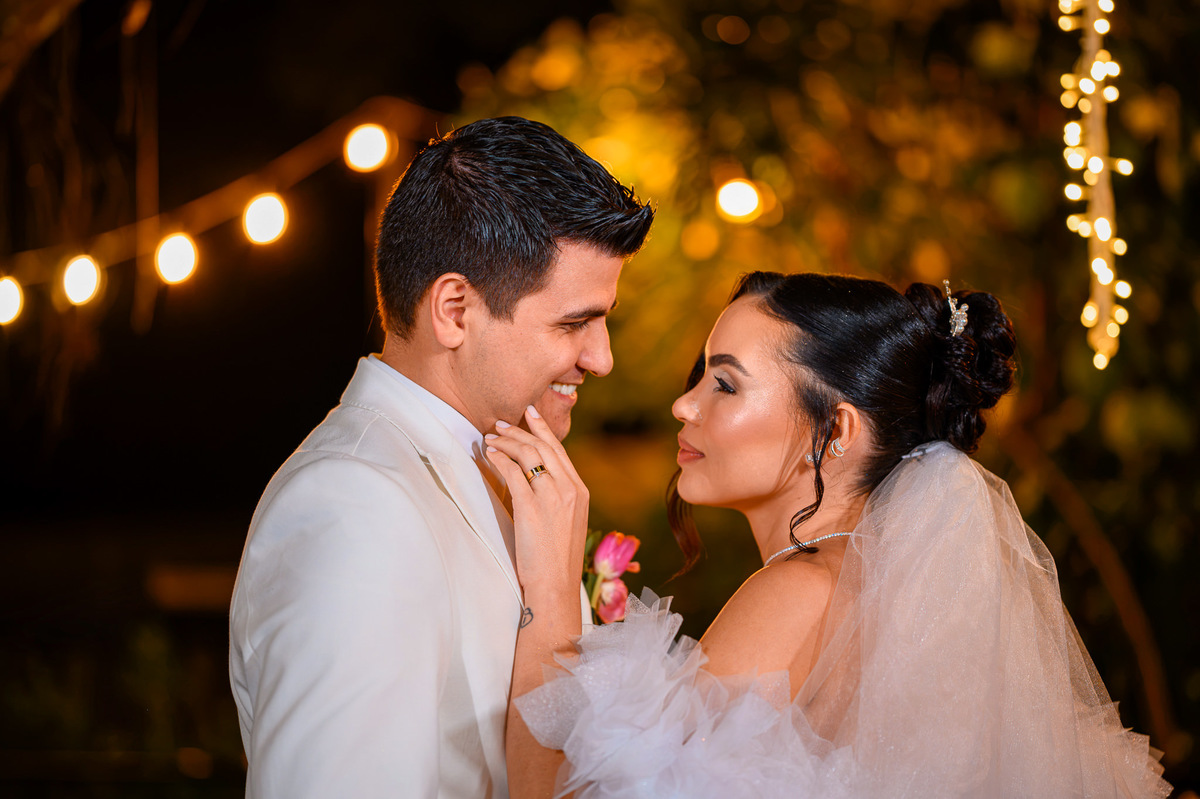 Noiva e noivo trocando olhares sob luzes no jardim

