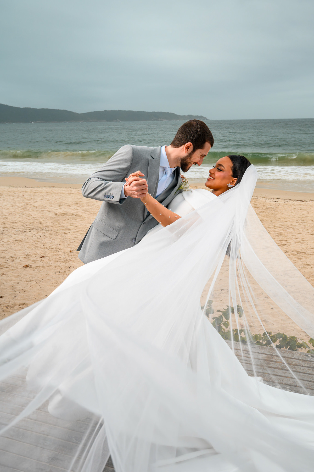 Noiva com vestido e véu estendidos diante do mar