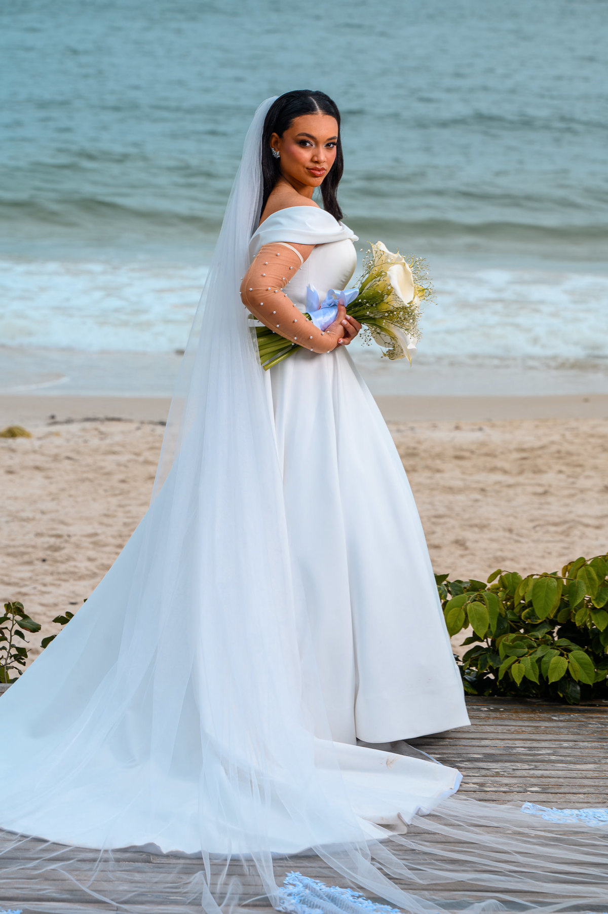 Noiva com buquê em retrato de corpo inteiro frente ao mar
