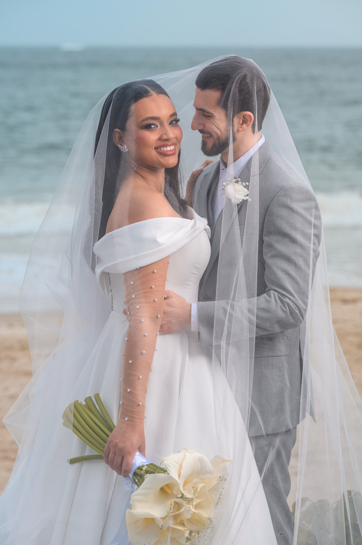  Casal envolvido pelo véu em frente ao mar