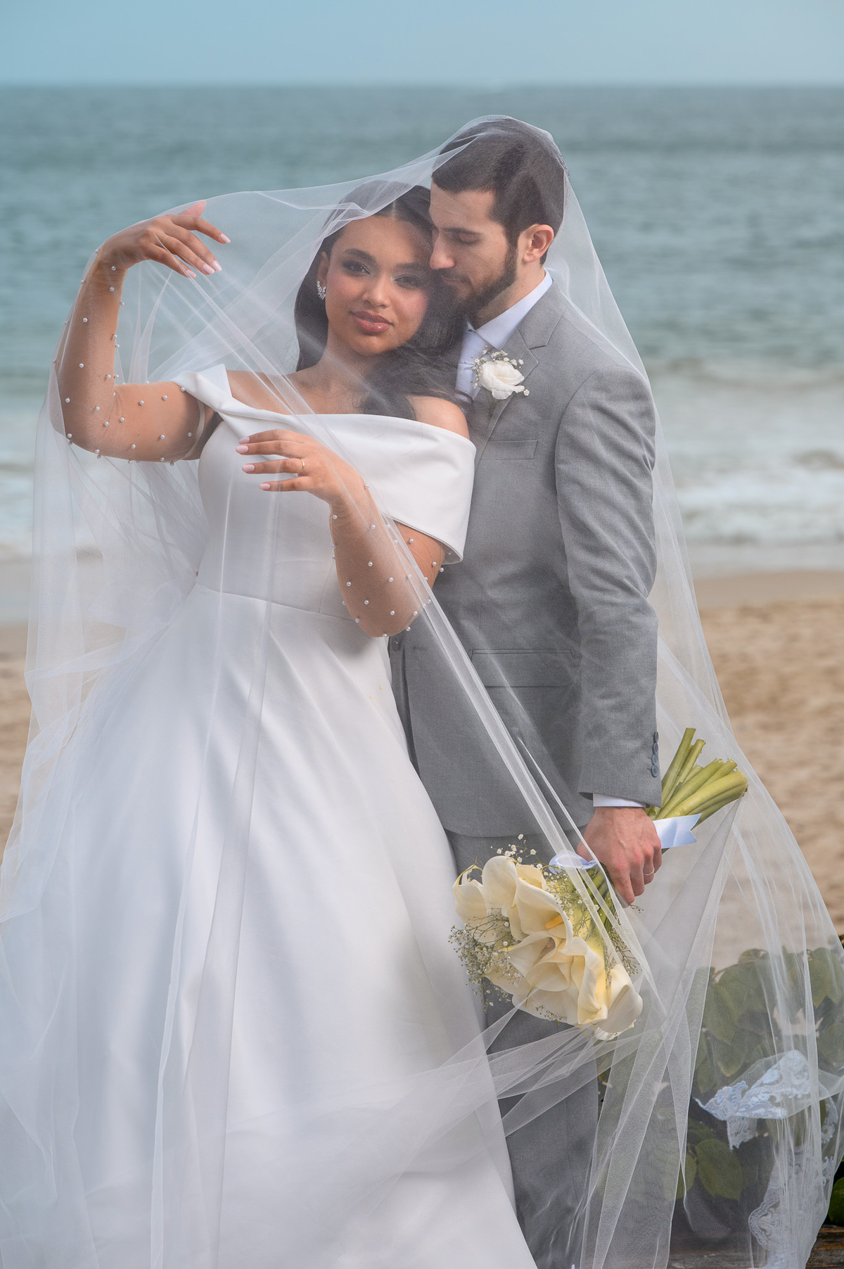 Noivos sob o véu em preto e branco na praia
