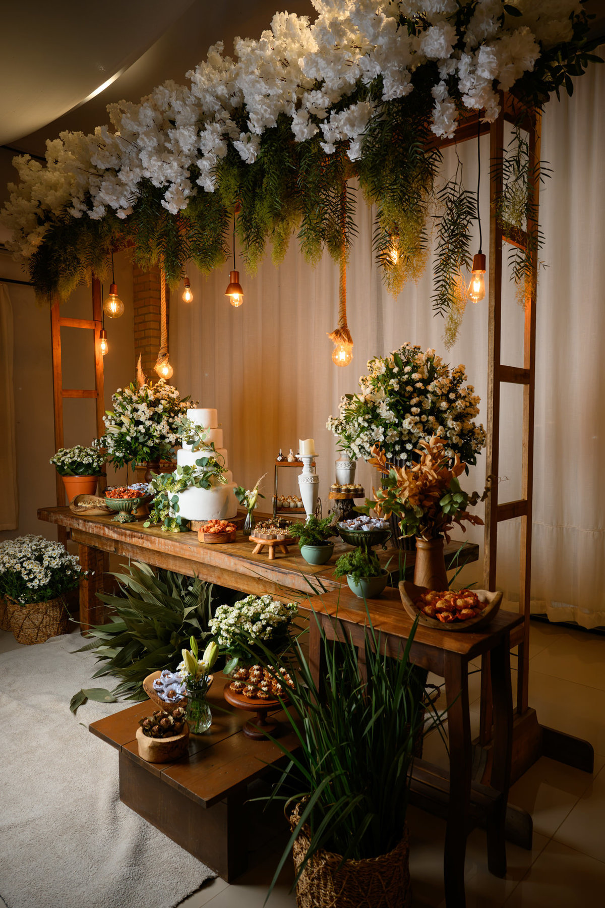Mesa de doces com decoração floral e luzes pendentes