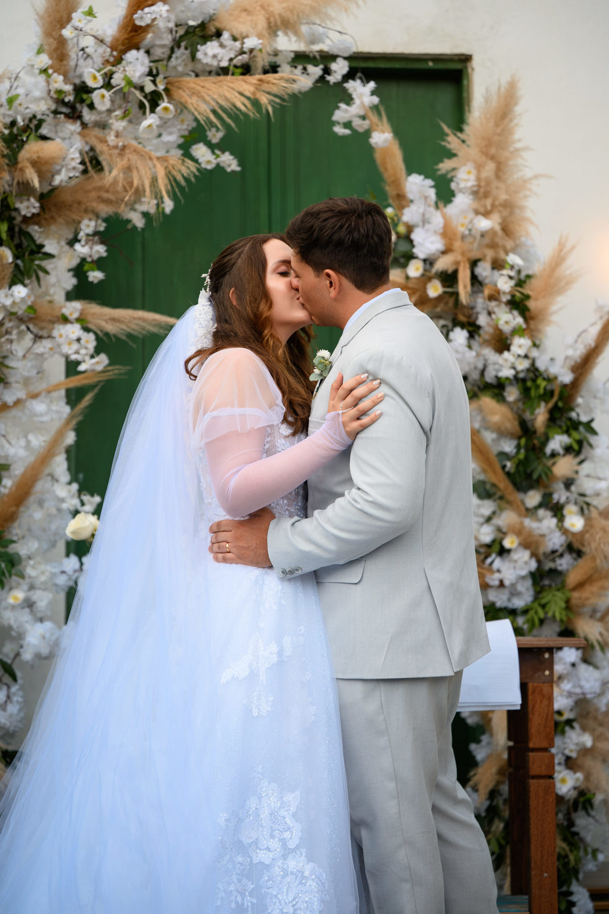 Beijo do casal diante da porta verde e decoração floral