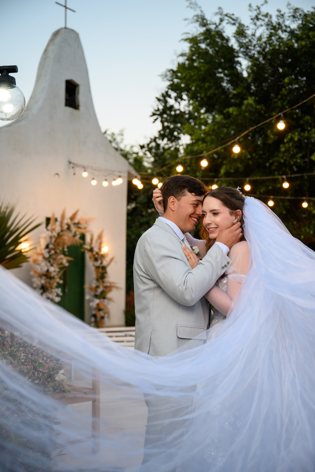 Casal com o véu em primeiro plano e capela ao fundo