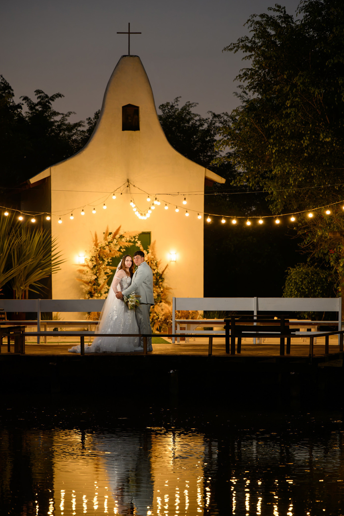 Casal e capela iluminada refletidos no lago do Vila Gomes