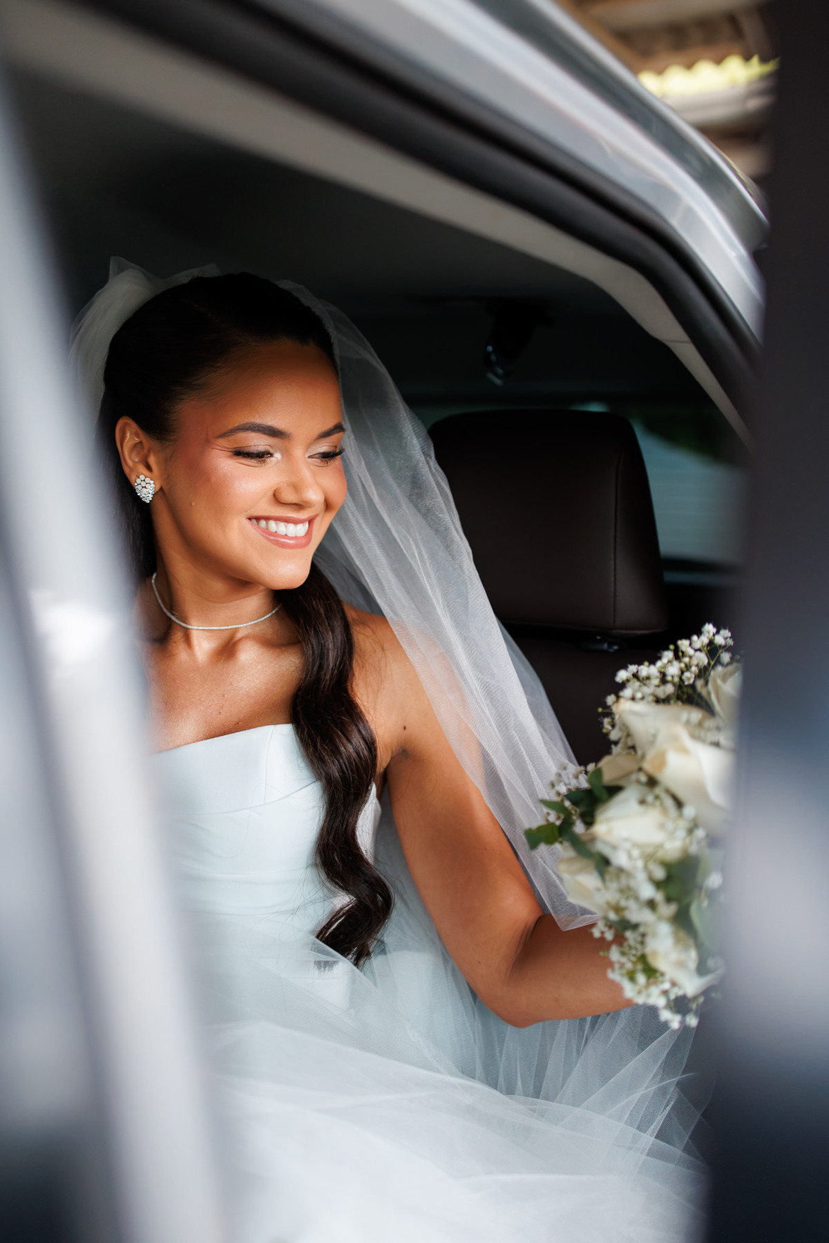 Noiva sorrindo dentro do carro com buquê antes da cerimônia