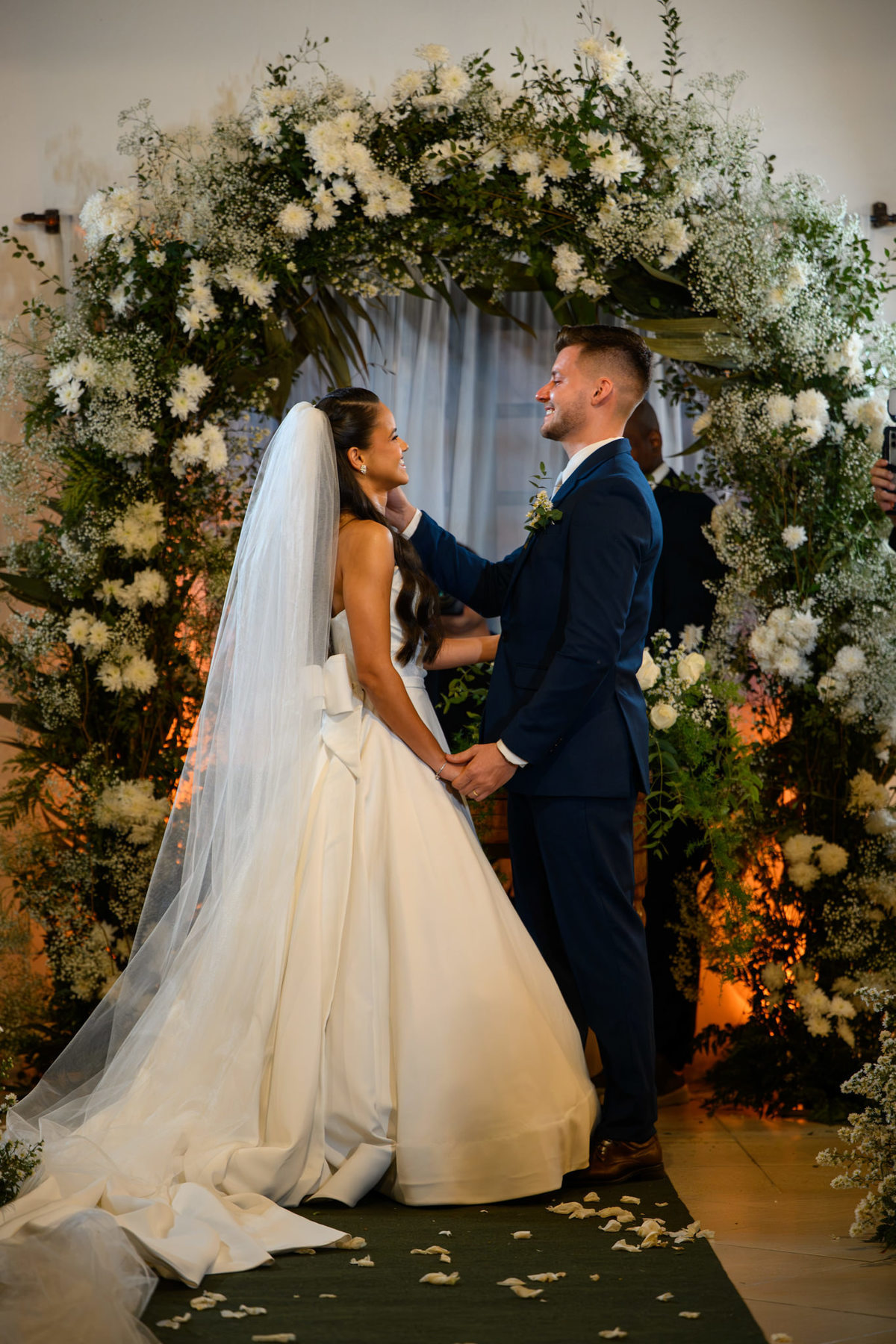 Noivos de mãos dadas diante do arco floral da cerimônia
