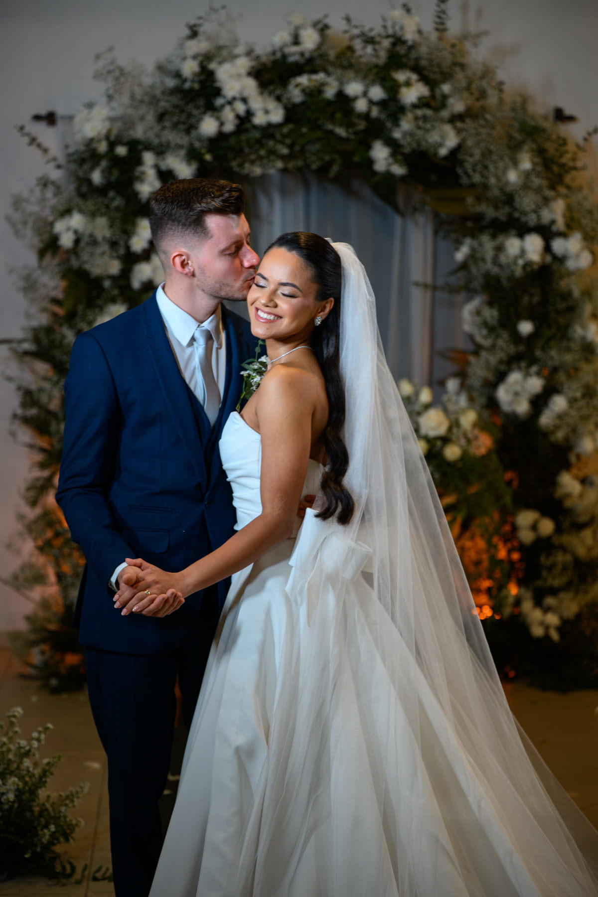  Casal sorrindo diante da decoração floral do casamento