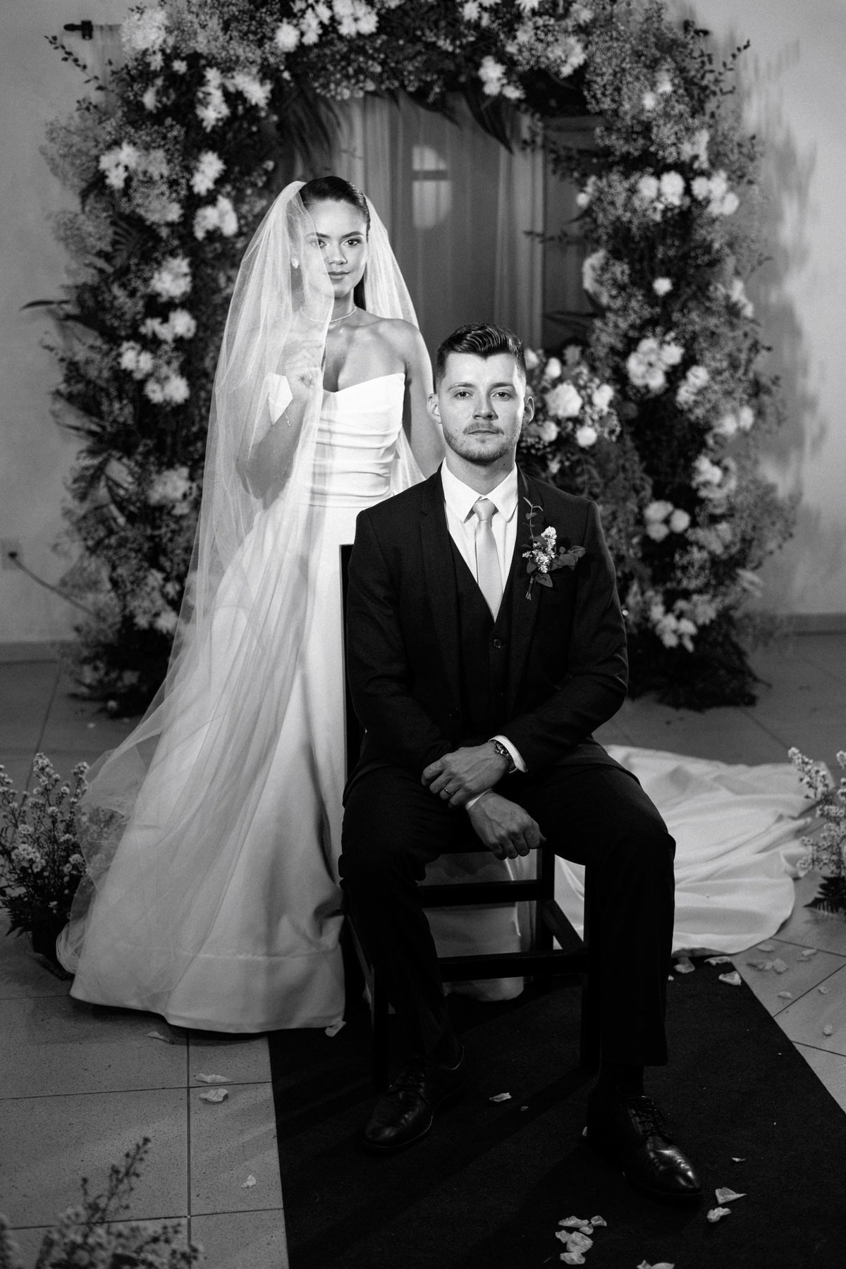  Retrato editorial em preto e branco com noivo sentado e noiva em pé