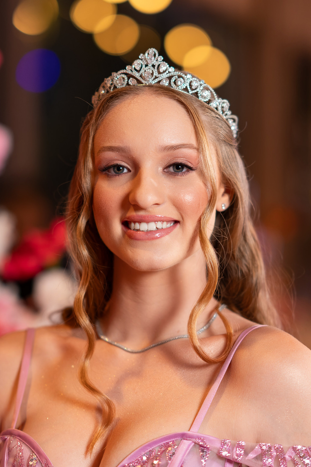 18. Close da debutante com tiara e luzes desfocadas ao fundo
