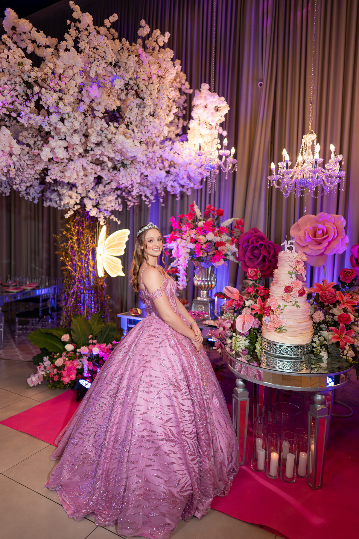 41. Debutante junto ao bolo, flores e árvore decorativa da festa de 15 anos
