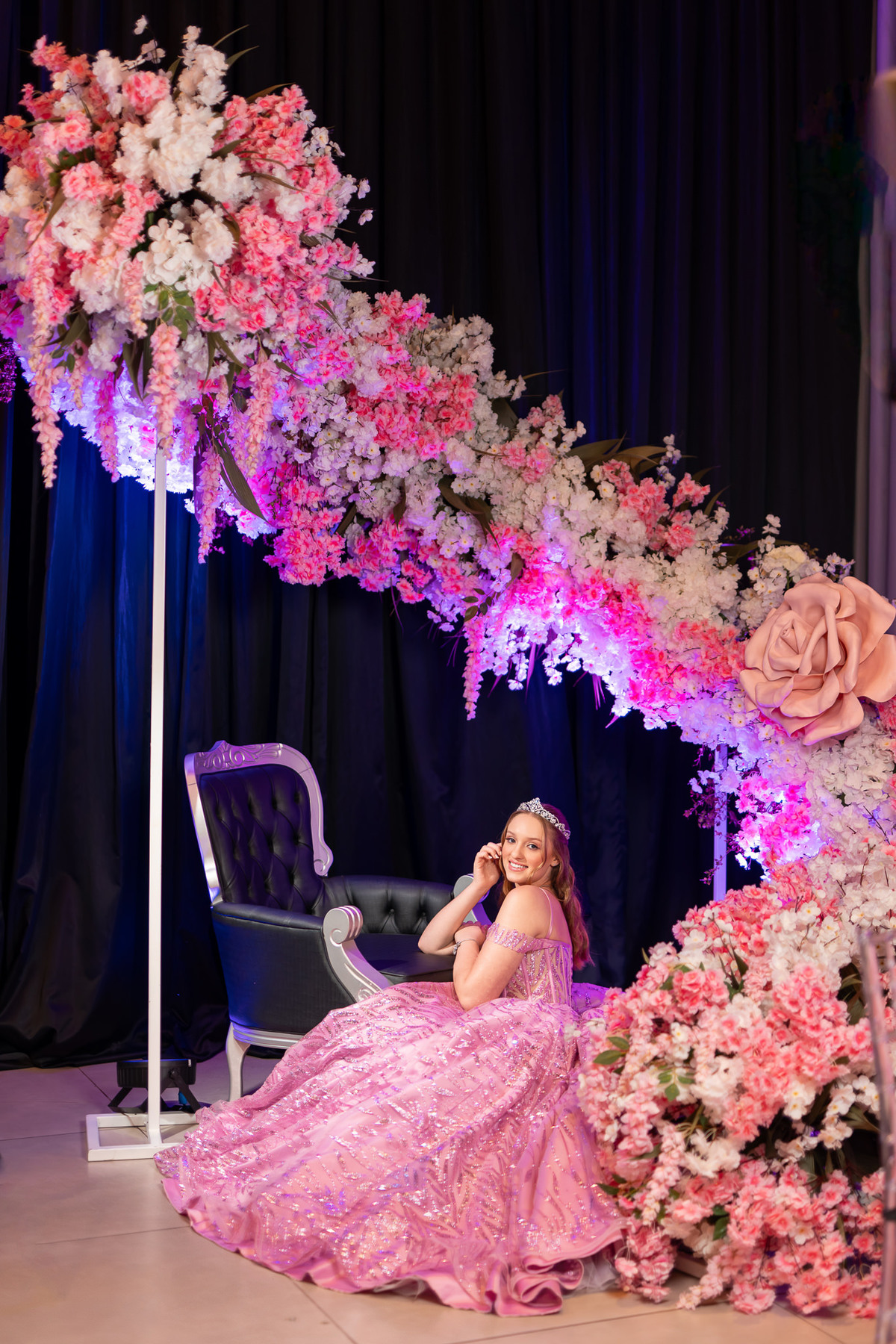 48. Debutante sentada sob grande arco de flores na decoração da festa
