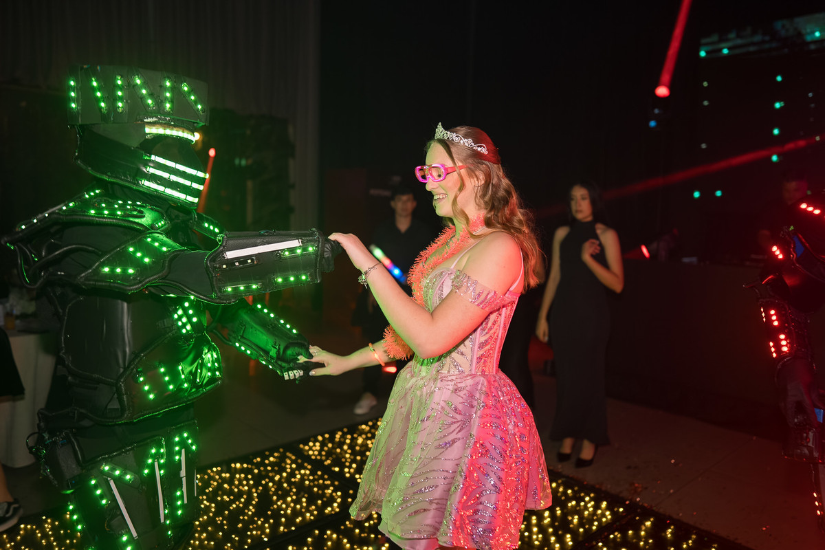 86. Debutante interagindo de perto com robô de LED durante a festa
