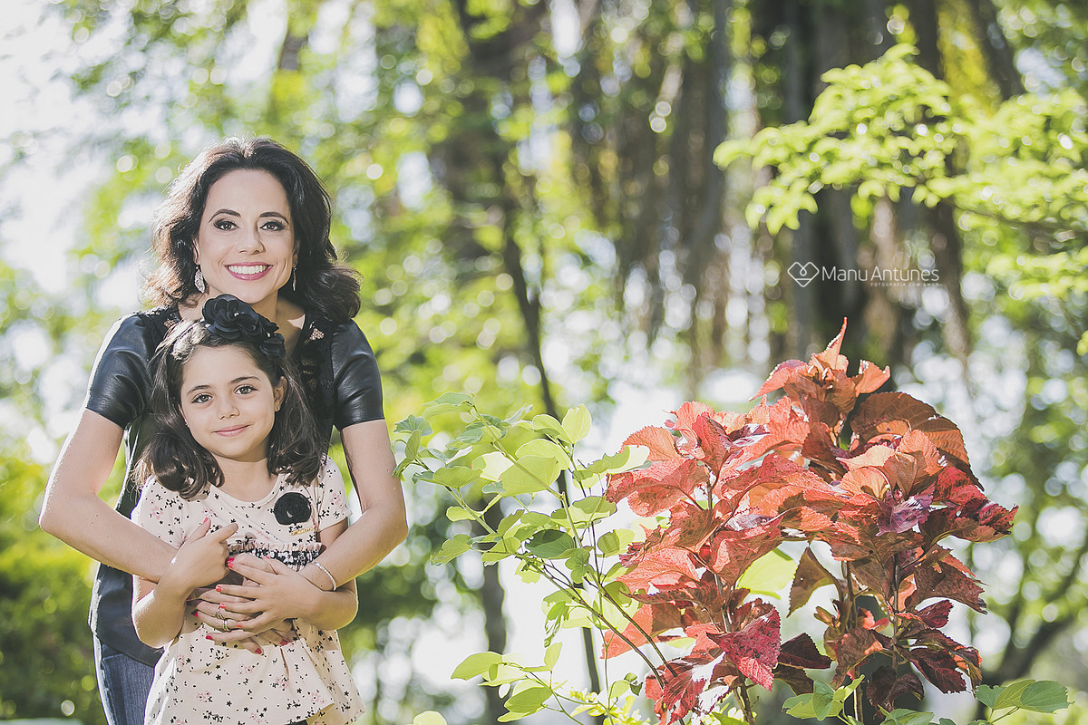 mãe e filha se abraçando perto da flor vermelha