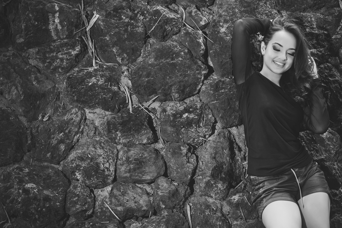 menina segurando o cabelo encostada no muro de pedra