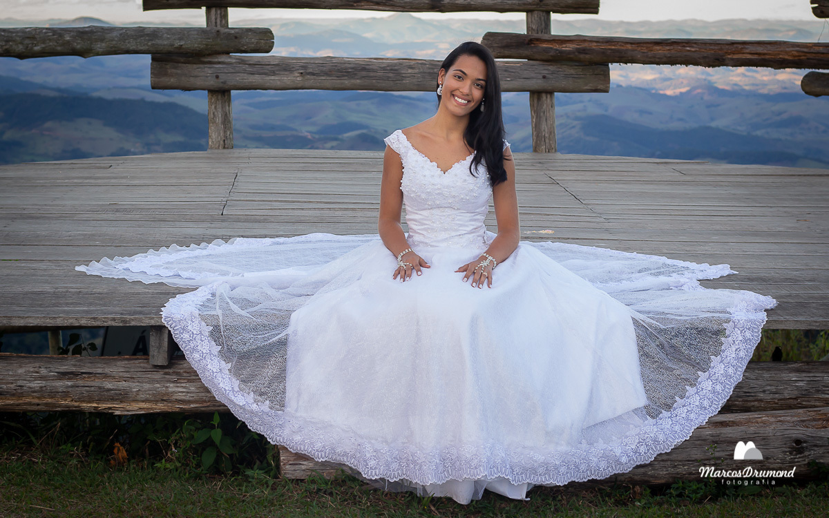 Noiva sentada com as mãos nas perns e o vestido bem detalhado entorno dela